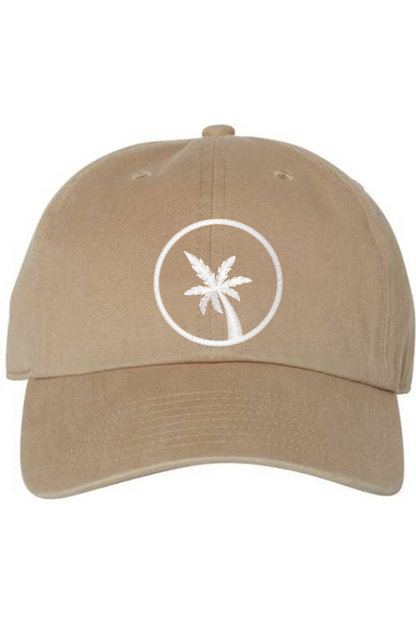 A khaki brown baseball cap with a curved brim. The front of the hat features an embroidered seven frond Palm Tree in white thread. The cap has a visible button on the top and an adjustable strap in the back (not visible).