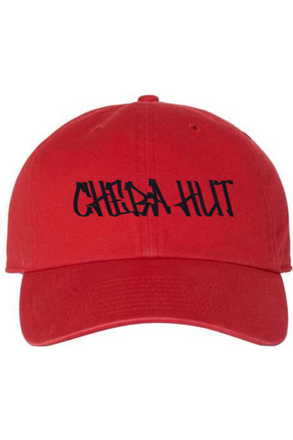 A red baseball cap with a curved brim. The front of the cap features the black stylized text 'CHEBA HUT' embroidered across the center. The cap has a visible button on the top and an adjustable strap in the back (not visible).