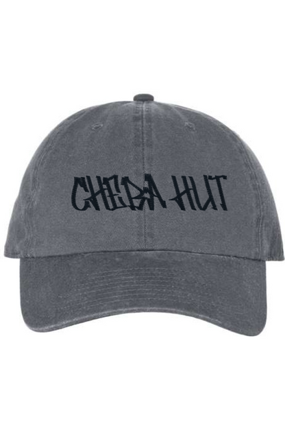A charcoal baseball cap with a curved brim. The front of the cap features the black stylized text 'CHEBA HUT' embroidered across the center. The cap has a visible button on the top and an adjustable strap in the back (not visible).