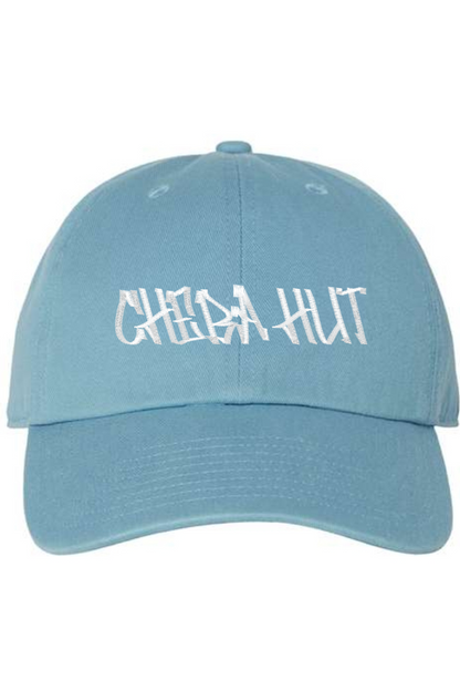 A blue baseball cap with a curved brim. The front of the cap features the white stylized text 'CHEBA HUT' embroidered across the center. The cap has a visible button on the top and an adjustable strap in the back (not visible).