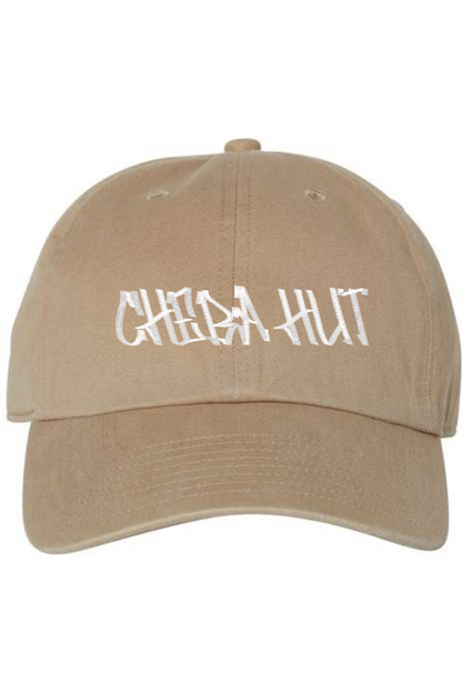 A khaki baseball cap with a curved brim. The front of the cap features the white stylized text 'CHEBA HUT' embroidered across the center. The cap has a visible button on the top and an adjustable strap in the back (not visible).