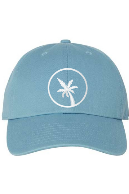 A blue baseball cap with a curved brim. The front of the hat features an embroidered seven frond Palm Tree in white thread. The cap has a visible button on the top and an adjustable strap in the back (not visible).