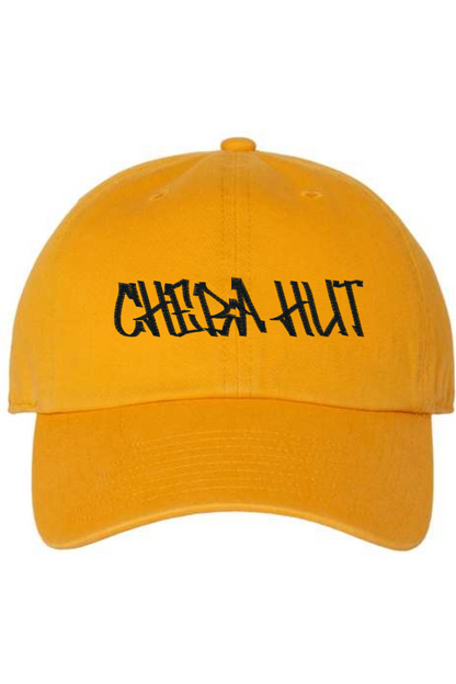 A gold baseball cap with a curved brim. The front of the cap features the black stylized text 'CHEBA HUT' embroidered across the center. The cap has a visible button on the top and an adjustable strap in the back (not visible).