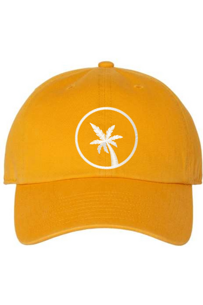 A gold baseball cap with a curved brim. The front of the hat features an embroidered seven frond Palm Tree in white thread. The cap has a visible button on the top and an adjustable strap in the back (not visible).