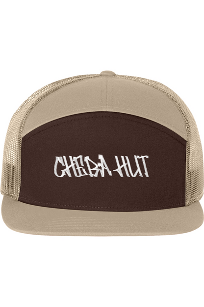 A seven-panel trucker hat with a solid dark brown front panel and a tan brim. The back two panels are tan mesh. The front of the hat features the white stylized text 'CHEBA HUT'. The hat has a slightly curved brim and a visible button on the top.