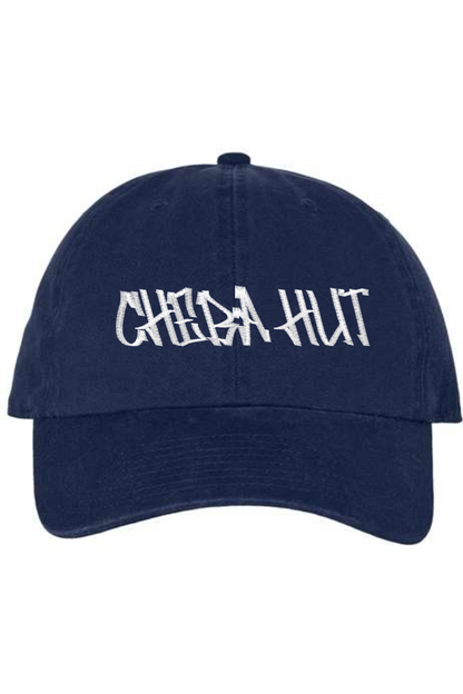 A navy baseball cap with a curved brim. The front of the cap features the white stylized text 'CHEBA HUT' embroidered across the center. The cap has a visible button on the top and an adjustable strap in the back (not visible).